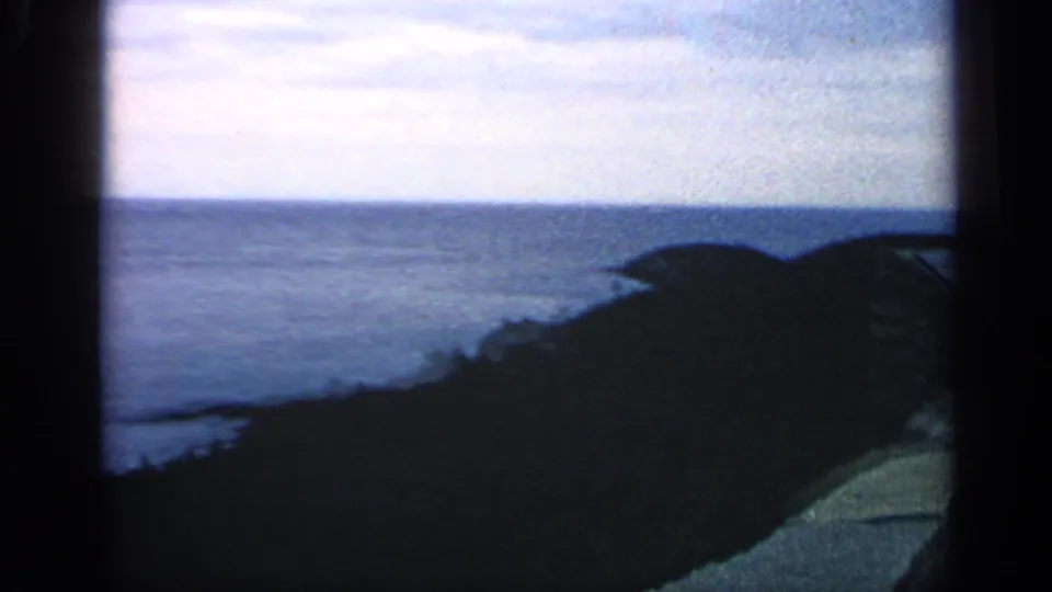 1968 8mm Massachusetts coastal view from a high bluff, with ocean horizon, cloudy sky, and dark hillside foreground.