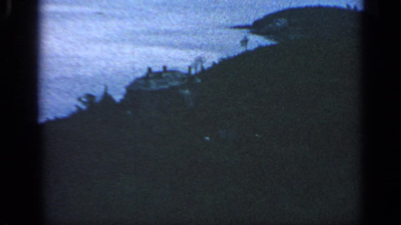 Hillside house silhouetted above water on a coastal bluff.