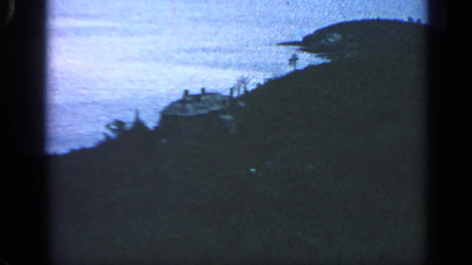 1968 8mm Massachusetts coastal home-movie frame showing a hillside house, surrounding vegetation, and water in the background.