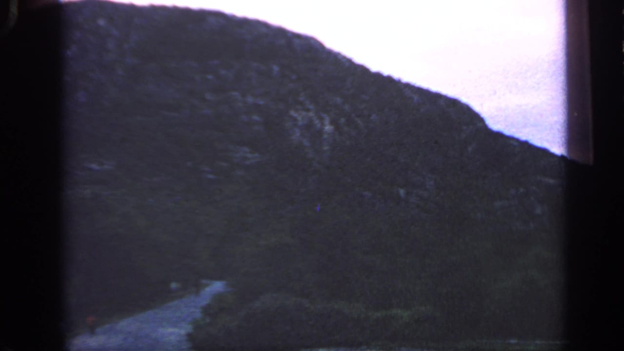Dark hillside above a coastal path and water under a pale dusk sky.