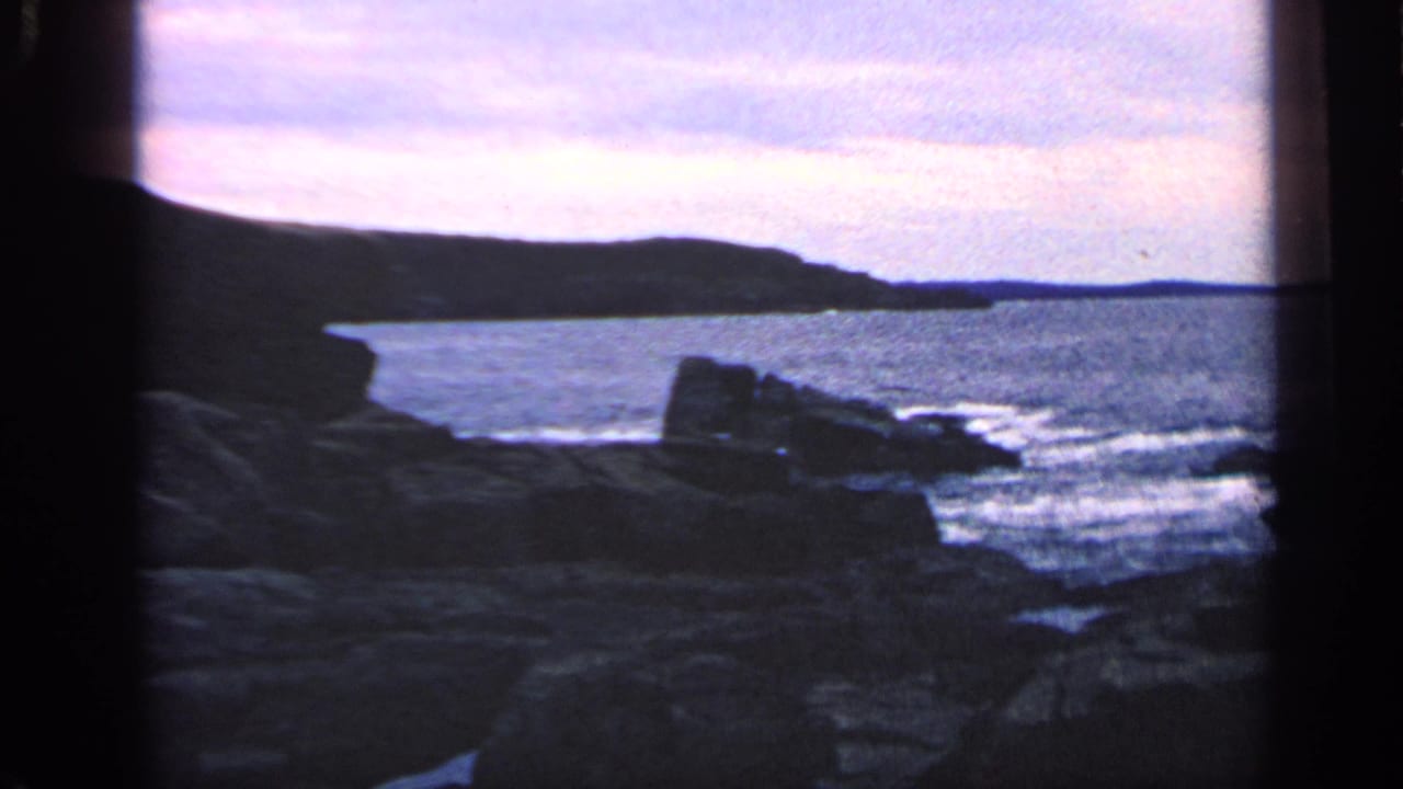 Rocky shoreline with waves under a pink dusk sky and dark film borders.