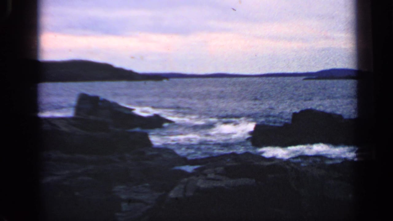 Open water and rocky outcrops with surf breaking near a distant shoreline.