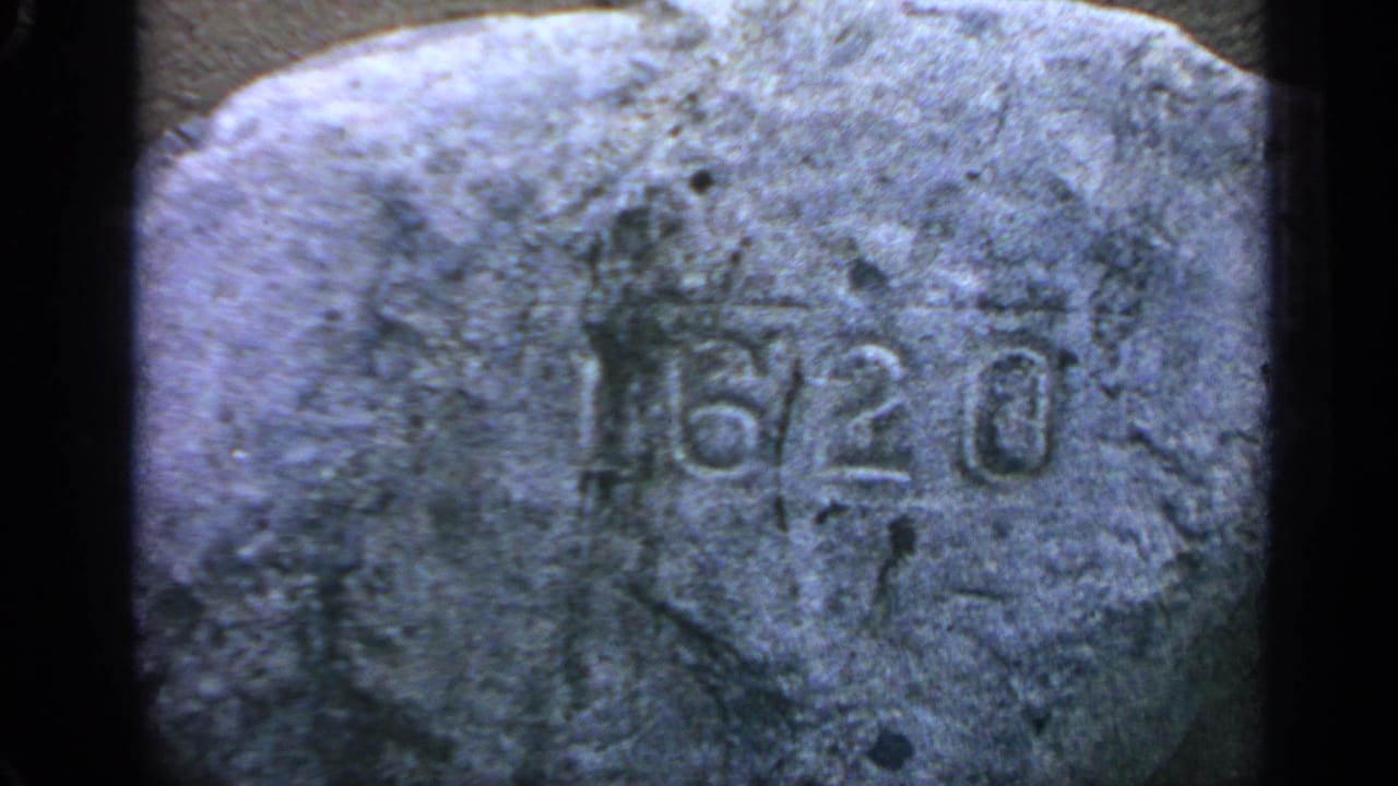 Close view of a weathered rock with 6/20 carved into its surface.