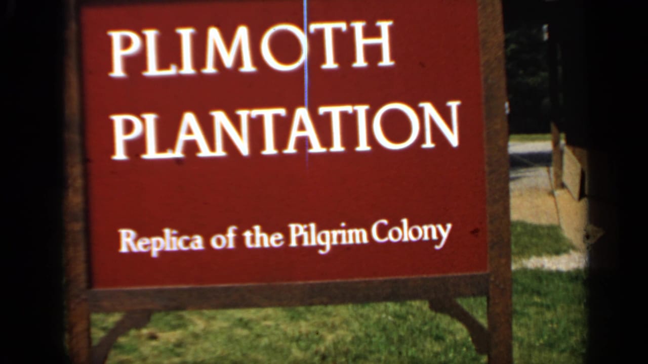 Red Plimoth Plantation sign beside grass and a dark film edge.