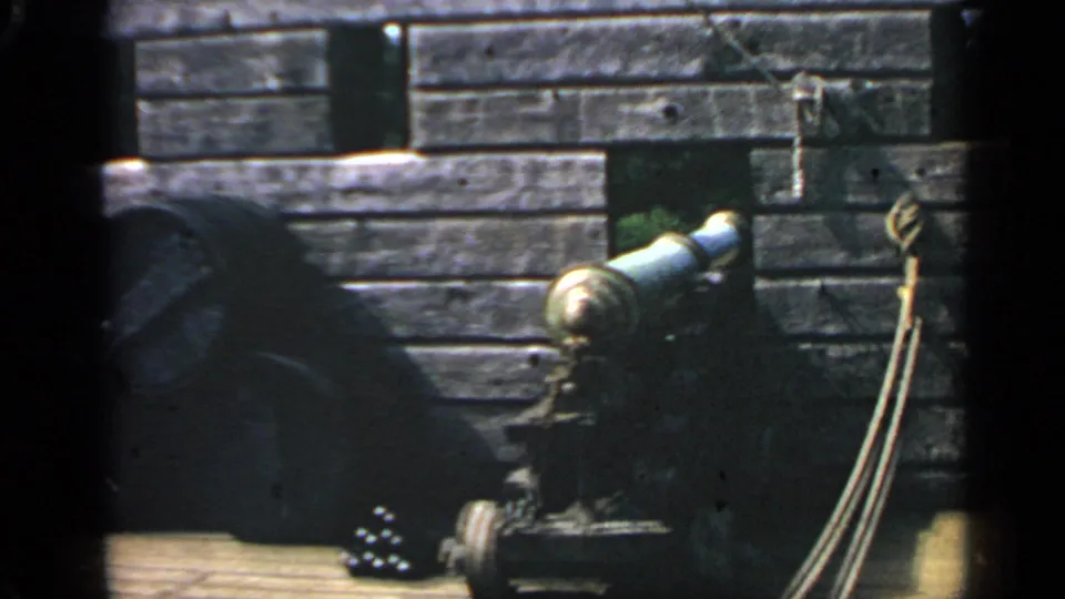 A cannon stands against a timber palisade wall at the Plimoth Plantation replica site in 1969 home-movie footage.