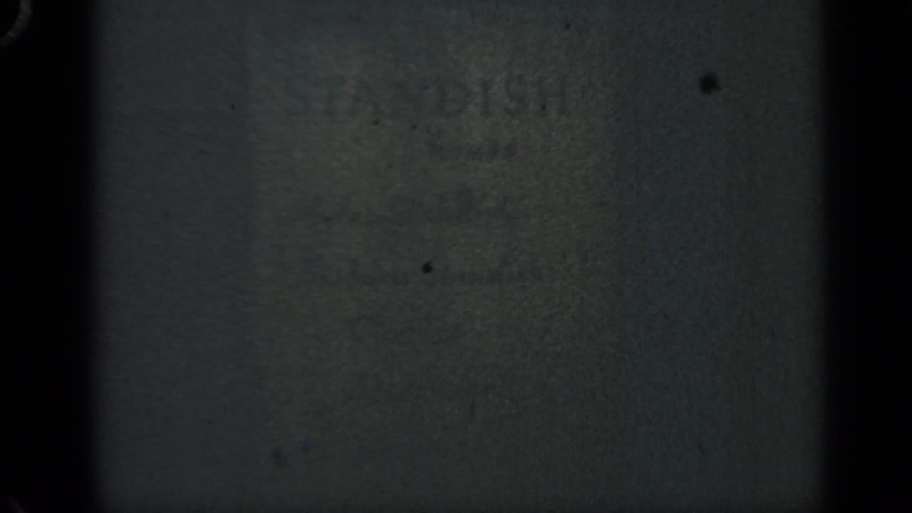 Dark 1969 Massachusetts 8mm frame with indistinct wall texture, soft focus, and visible film wear.