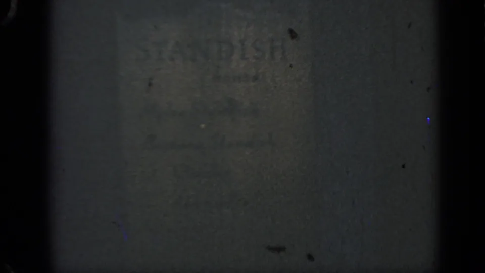 1969 Massachusetts 8mm frame showing faded STANDISH lettering on a textured wall with grain and shadow.