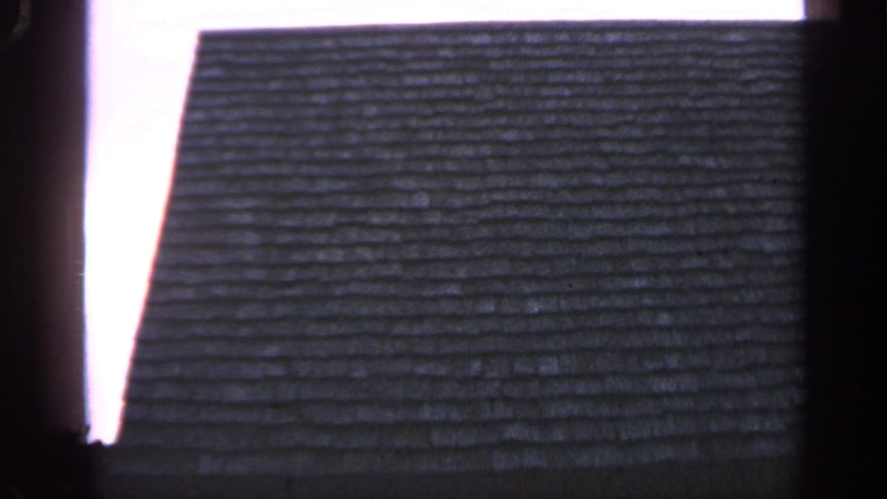 The zoom reveals part of a weathered shingled roof with a bright sky edge and dark frame border.