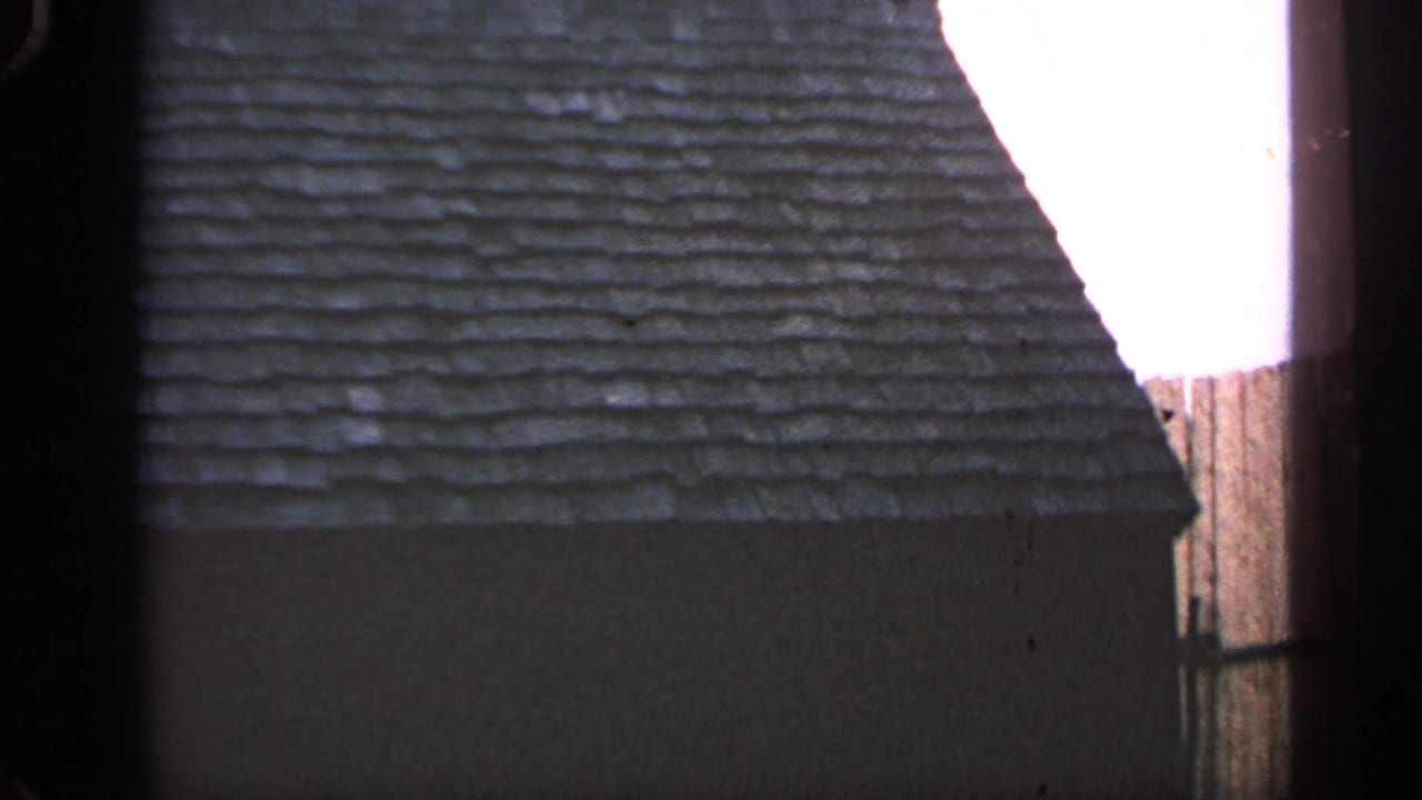 Close 8mm view of the cottage roof and wall in Massachusetts, divided by a dark vertical obstruction or film edge.