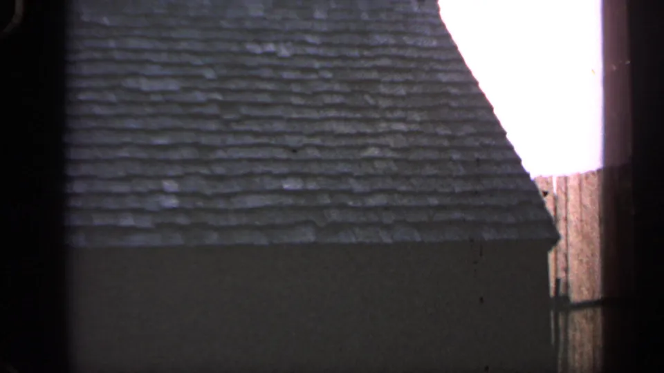 Close 8mm view of the cottage roof and wall in Massachusetts, divided by a dark vertical obstruction or film edge.