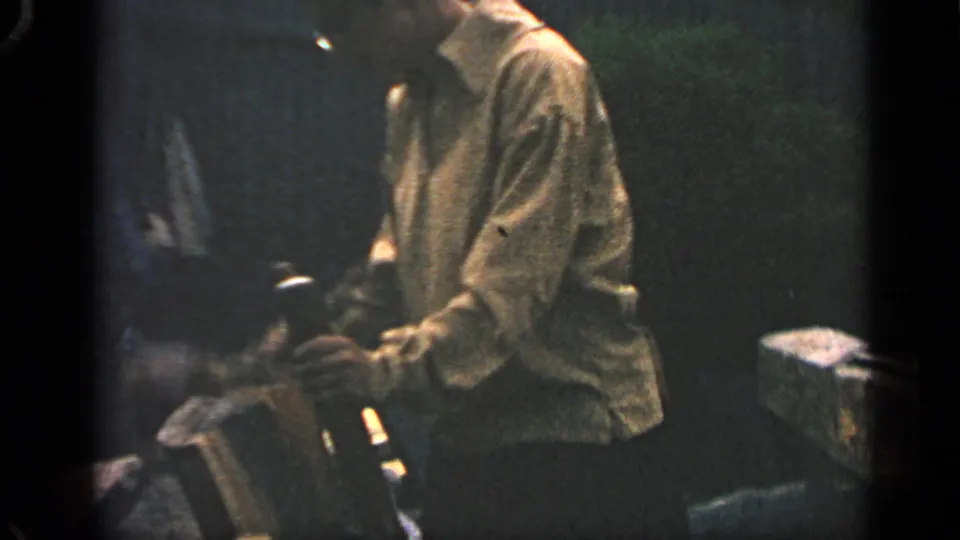 Close 8mm frame from the 1969 Massachusetts clip showing a man in a light shirt handling wood or tools in shadow.