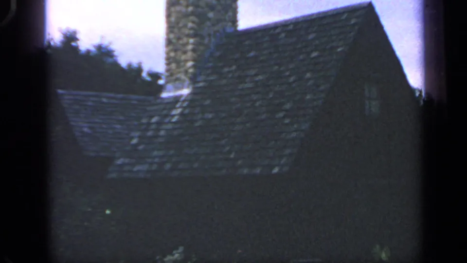 1969 Massachusetts 8mm frame showing a dark shingled roof, stone chimney, trees, and pale sky.