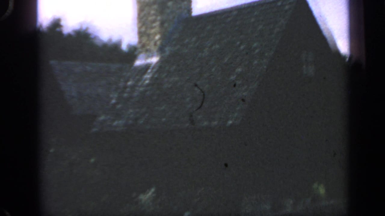 Dark house exterior with stone chimney and trees, partly obscured by film-frame shadow.