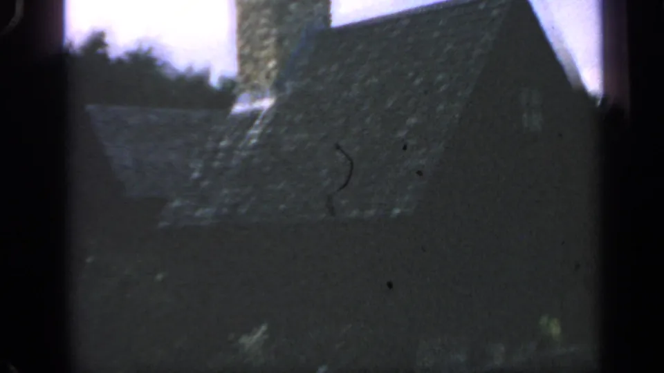 Massachusetts 1969 8mm frame showing a dark New England-style house with a stone chimney, trees, and heavy edge shadow.