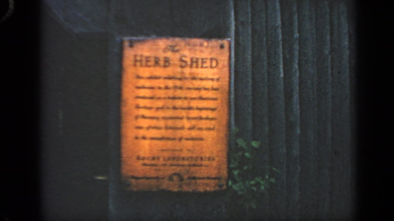 Orange Herb Shed plaque mounted on a dark wooden wall beside vertical boards and greenery.