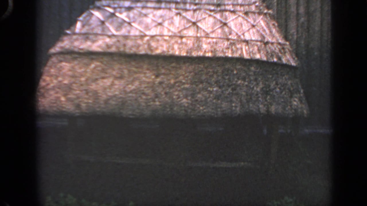 Thatched roof section with crisscross wooden framework above a dark wall.