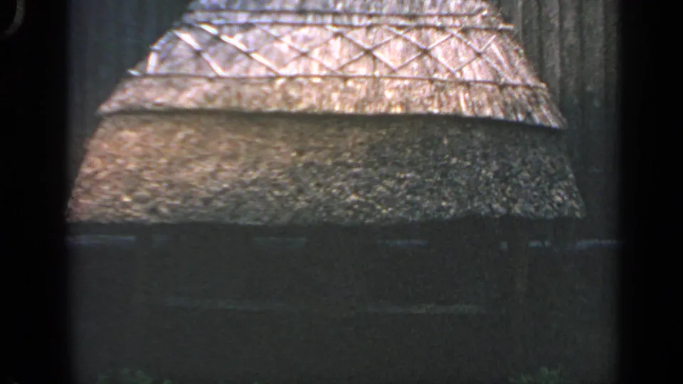 1969 Massachusetts home-movie frame with a close view of the thatch texture, crossed wooden band, and shaded structure below.
