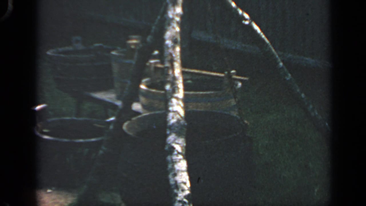 1969 Massachusetts 8mm frame showing buckets, a large pot or cauldron, and a tripod-like support in a shaded outdoor display.