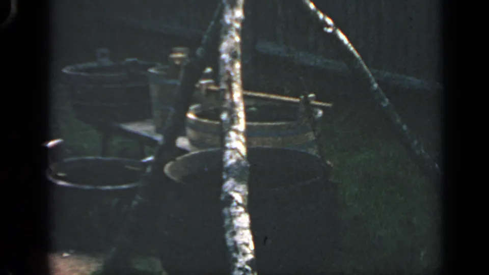 1969 Massachusetts 8mm frame showing buckets, a large pot or cauldron, and a tripod-like support in a shaded outdoor display.