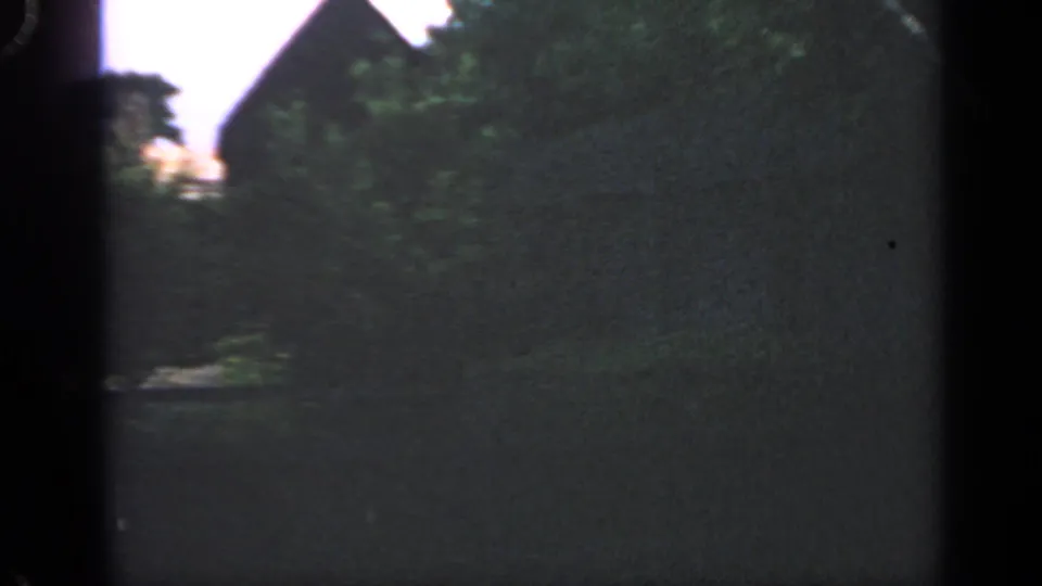 1969 Massachusetts 8mm frame showing a shaded path or clearing with greenery and part of a dark structure nearby.