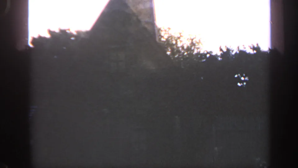 1969 Massachusetts 8mm frame showing a dark stone structure with a steep upper section, treetops, and overexposed sky.
