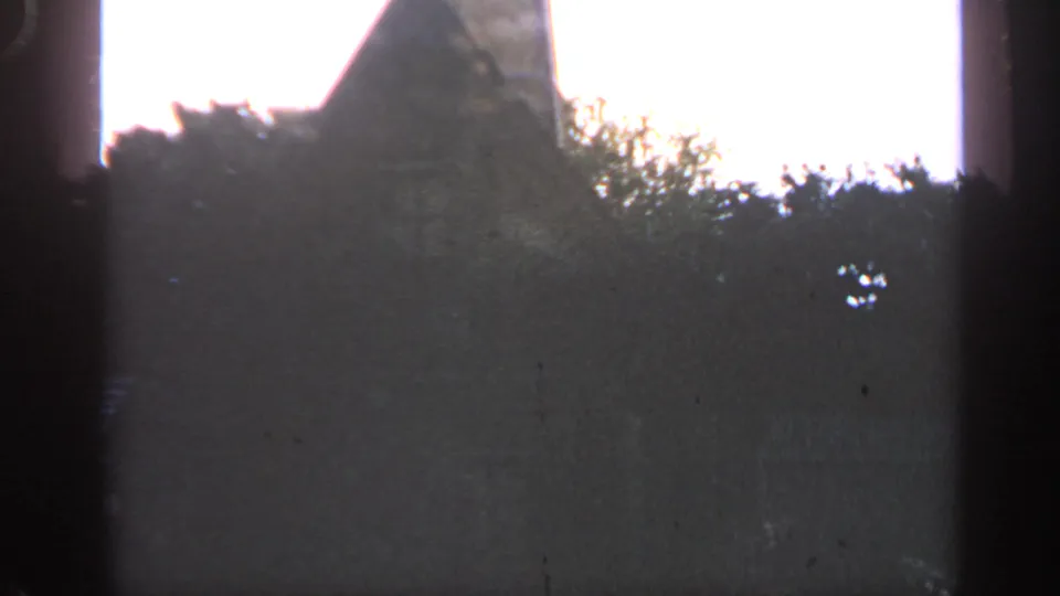 1969 Massachusetts 8mm frame of a dark stone roofline and surrounding trees, with bright sky and visible film-edge shadows.
