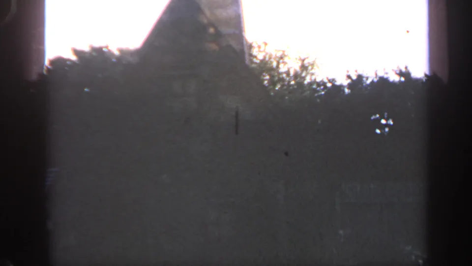 Massachusetts 1969 8mm frame showing a dim, partially obscured rural structure line behind trees under a bright sky.