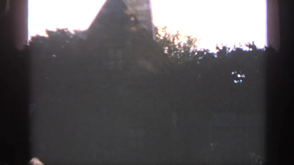 Massachusetts 1969 8mm view of a backlit rural roofline or structure edge partly hidden by trees and film gate shadows.
