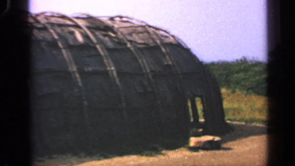 Massachusetts 1969 8mm frame showing a rustic dome-shaped building with curved ribs, a dark opening, grass, and distant trees.