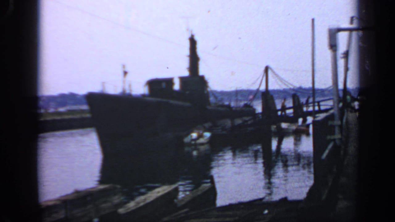 Large submarine moored beside a wooden pier in calm harbor water.