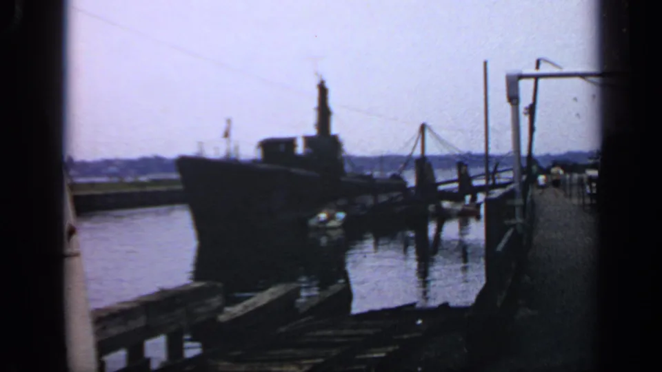 Dockside 8mm view of a submarine in Massachusetts, with pier structures, reflective water, and a bright horizon.