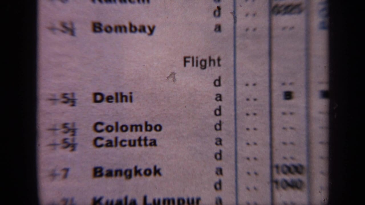 Close-up of a printed flight schedule listing Bombay, Delhi, Colombo, Calcutta, and Bangkok.