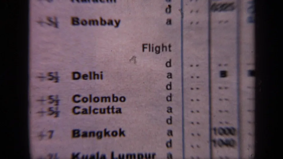 1970 India 8mm frame showing a close-up flight schedule with destination names and columns on aged paper.
