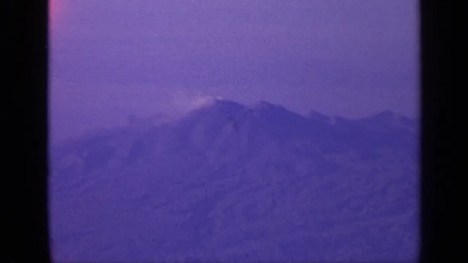 Grainy 8mm landscape frame from India showing distant mountains under a cloudy, purple-tinged sky.