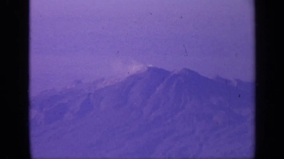 1970 India 8mm frame showing hazy snow-capped mountain peaks from a passenger aircraft, with purple color shift and film grain.