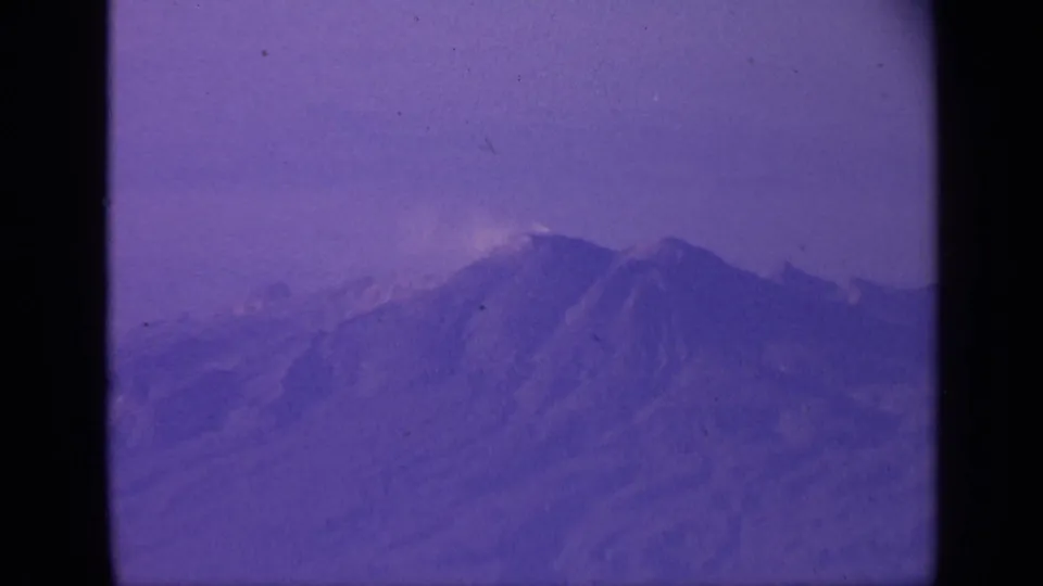 High-altitude 8mm view over mountains in India, with soft haze, purple film tint, and dark aircraft-window framing at the side.