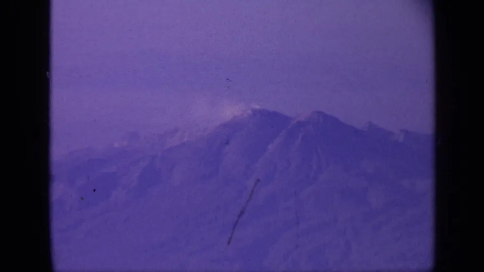 1970 India travel frame with distant mountain peaks filmed from a plane, showing soft focus, purple color shift, grain, and a scratch mark.