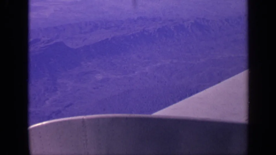1970 India aerial home-movie frame with the airplane wing in the foreground and layered ridges fading into haze.