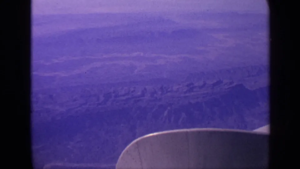 1970 India home-movie frame with a purple-tinted aerial view of dry ridges and the airplane wing in the foreground.