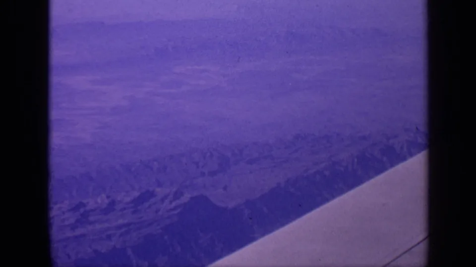 1970 India 8mm frame looking down at rugged arid mountains with an airplane wing cutting across the foreground.
