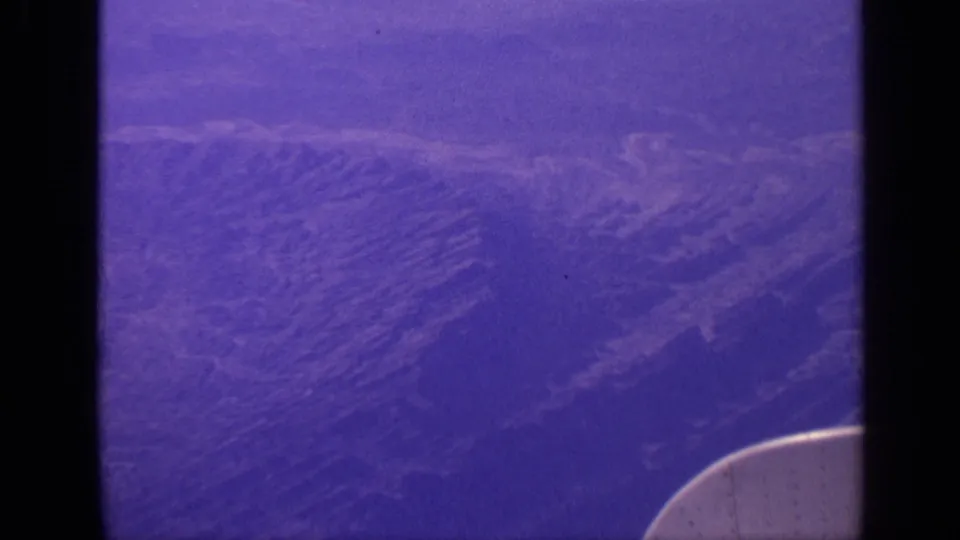Vintage 8mm aerial view over mountainous terrain in India, framed by airplane-window shadows and an aircraft edge at lower right.