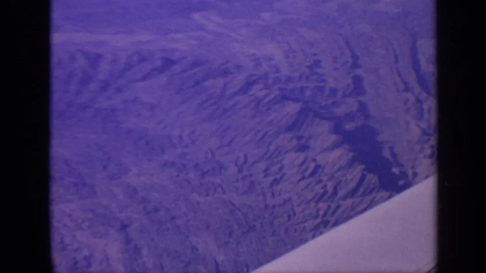 1970 India aerial 8mm view of rugged mountain slopes and valleys, with the airplane wing edge crossing the lower right of the frame.