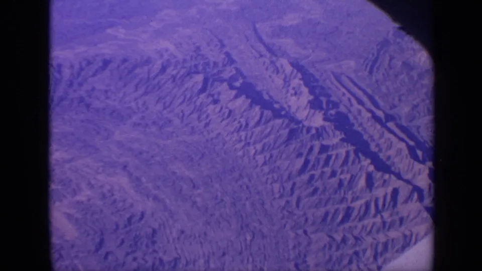 1970 8mm frame showing a purple-blue surface-like subject with ridge patterns, dark channel forms, and visible small-gauge frame edges.