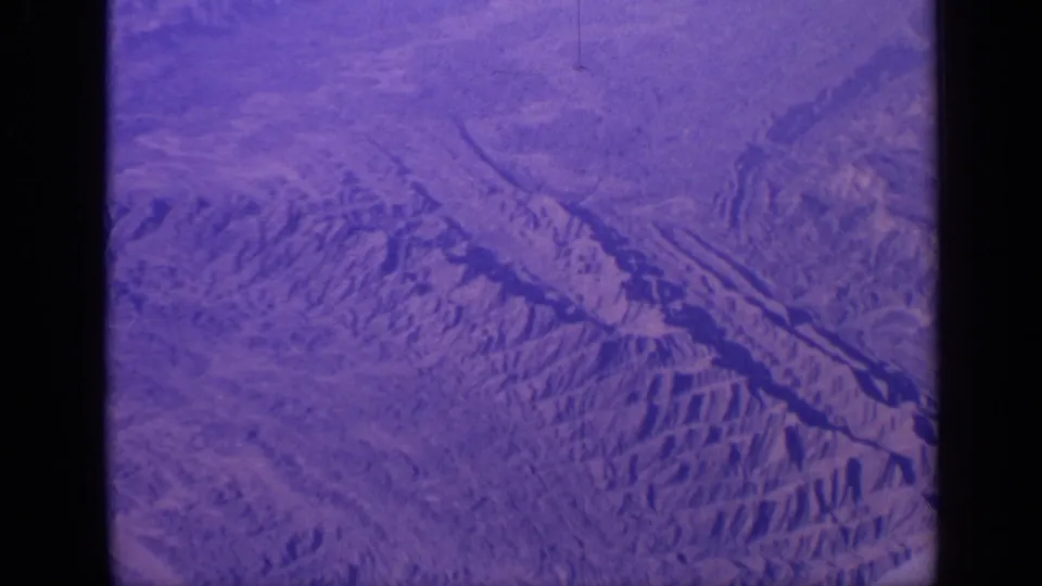 Aerial 8mm frame from India showing a broad dry mountain landscape with ridges, valleys, and aged purple color shift.