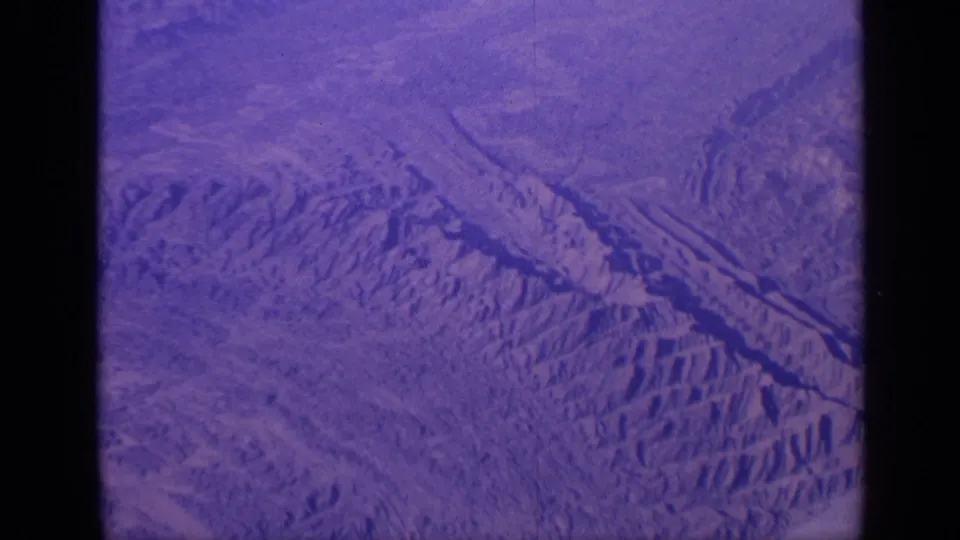 1970 India aerial home-movie frame showing oblique mountain ridges, dry valleys, and visible 8mm contact-sheet divider.