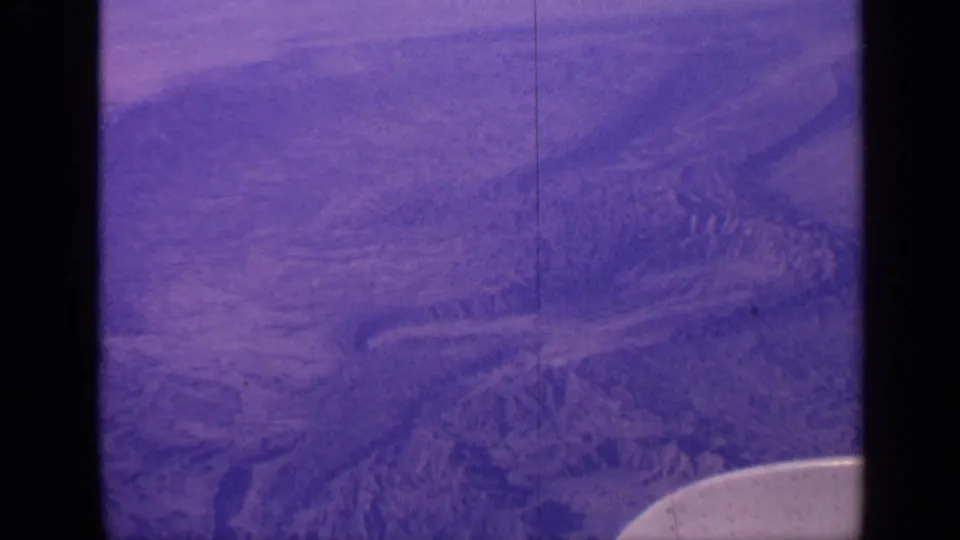 1970 India 8mm frame looking down from an aircraft over ridges and valleys, with visible film borders, scratches, and wing edge.