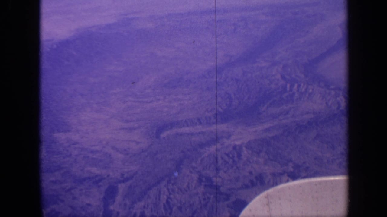 1970 India 8mm aerial view showing mountainous terrain and valleys below, with aged purple-blue film color.