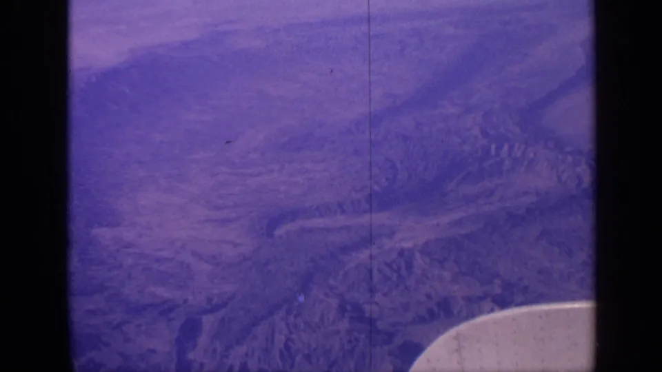 1970 India 8mm aerial view showing mountainous terrain and valleys below, with aged purple-blue film color.