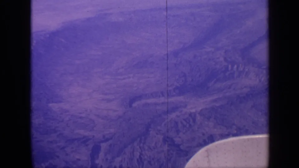 1970 India aerial home-movie frame with rugged terrain below and a pale airplane wing edge visible at lower right.