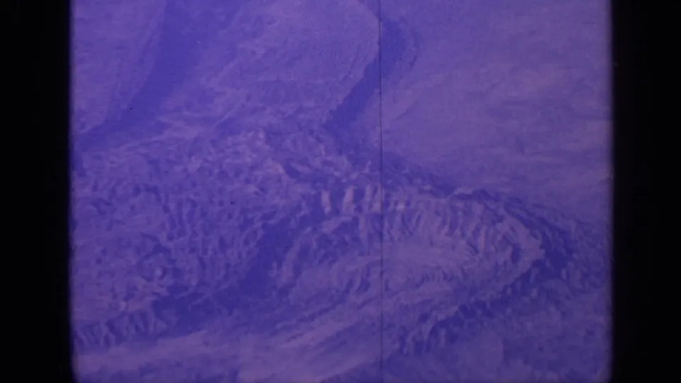 Aged 8mm aerial frame from India in 1970, showing ridged mountain terrain through a passenger airplane window.